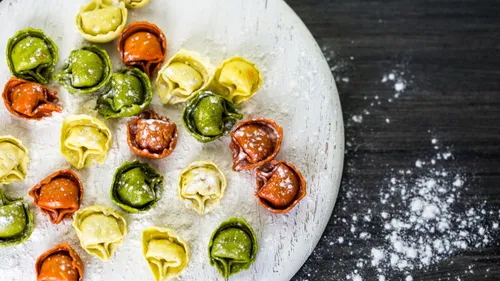 Colorful tortellini on a floured round surface.