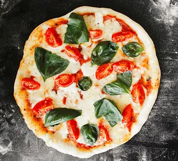 Pizza with tomatoes and basil on black surface.