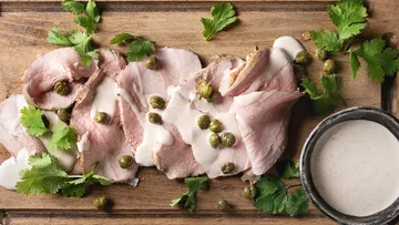 Geschnittenes Fleisch mit Soße und Kräutern auf Brett.