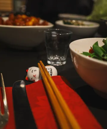 Chopsticks on red cloth beside bowls and utensils.
