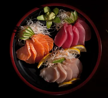 Sashimi-Platte mit Avocado-Garnitur auf schwarzem Teller.