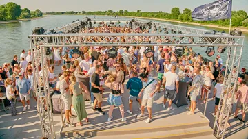 People partying on a riverboat under sunny sky.