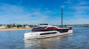 Modern ship sailing on river near bridge.