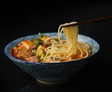 Chopsticks lift noodles from soup bowl.
