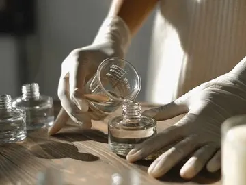 Eine Hand gießt Flüssigkeit in ein Glasfläschchen auf einem Tisch.