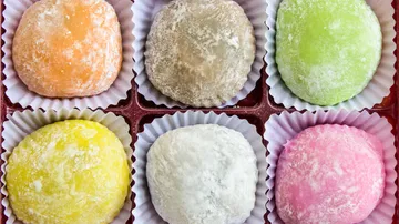 Six colorful mochi in paper cups, top view.