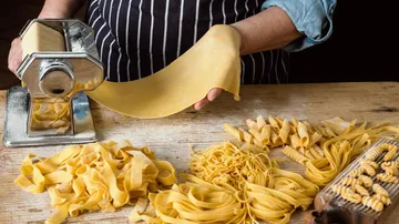 Person using pasta machine on wooden table.