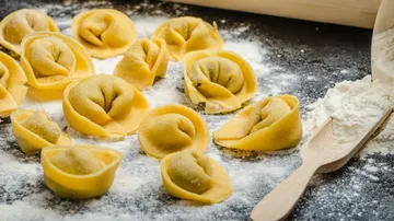 Fresh tortellini on floured surface with flour scoop.