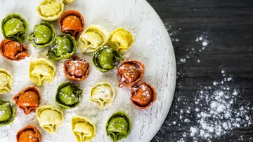Colorful tortellini arranged on floured wooden board.