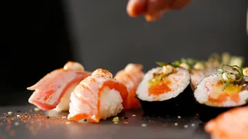 Hand seasoning sushi pieces on black plate.