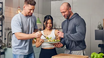 Three people enjoying food in kitchen.