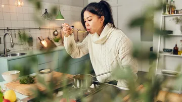 Frau probiert Suppe in moderner Küche.