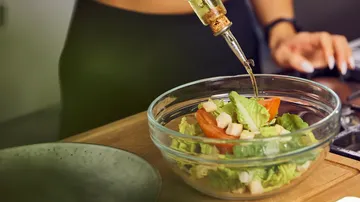 Salat in einer Schüssel, Dressing wird hinzugefügt.