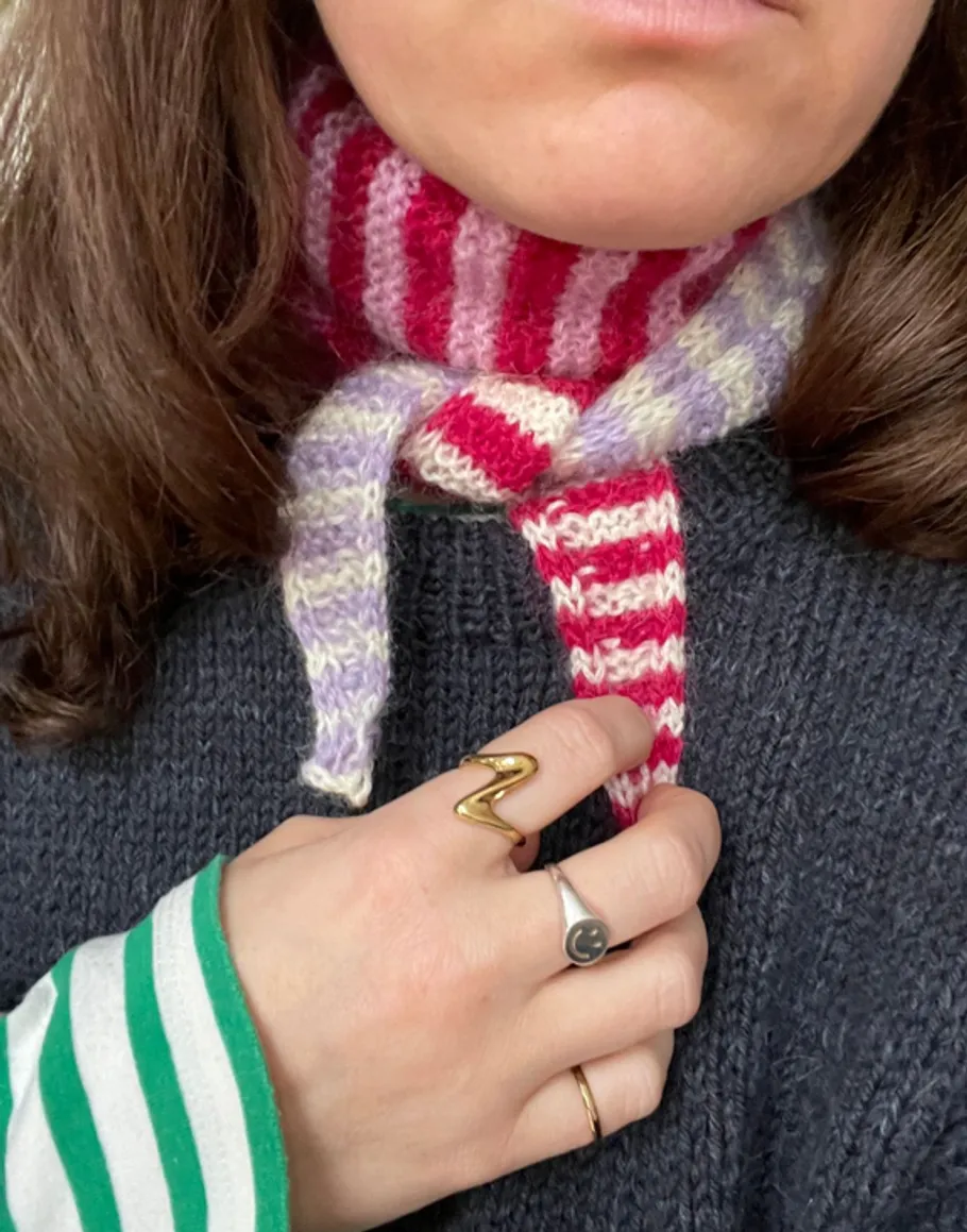 Striped scarf around neck, hand with rings visible.