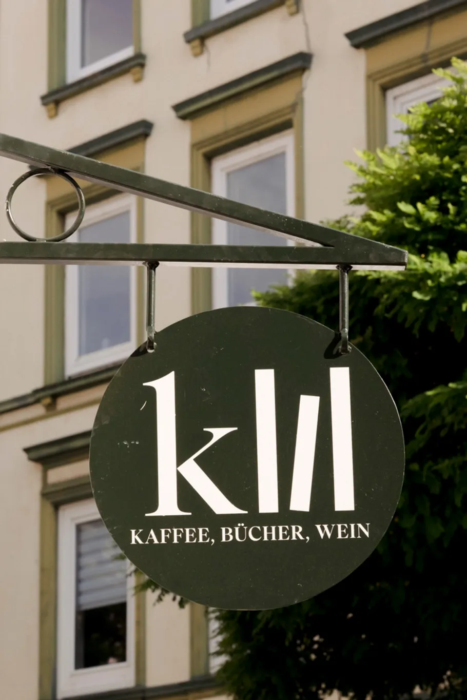 Ladenschild mit Text, Gebäude dahinter.