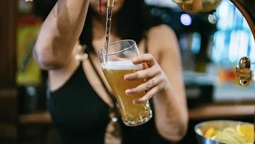 Person schenkt Bier in ein Glas an der Bar ein.