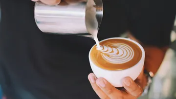 Person gießt Latte Art in Kaffeetasse.