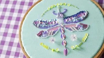 Perlenglücklibelle Stickerei auf Stoffrahmen.