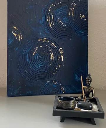 Buddha figurine and incense in front of abstract painting.