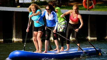 Four women paddleboard together on a river.