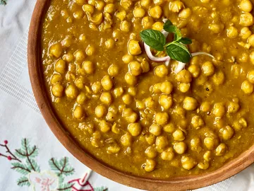 Kichererbsencurry, garniert mit Kräutern, auf Tisch.