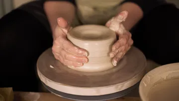 Hands shaping clay on a pottery wheel.