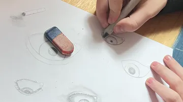 Hands drawing eyes on paper at table.
