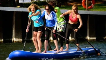 Four women paddleboarding on a river.