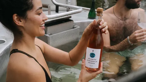 Lächelnde Frau hält Flasche im Whirlpool.
