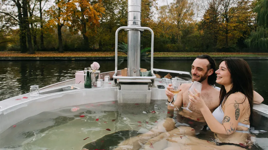 Couple relax in hot tub on lake.