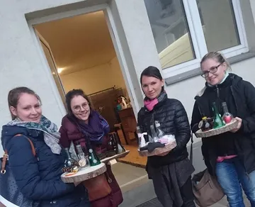 Vier Frauen halten Tabletts mit Flaschen draußen.