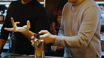 Two people mixing drinks at a bar.