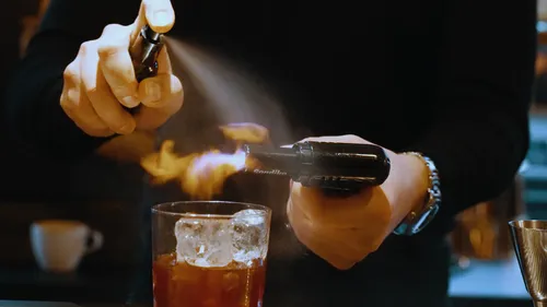 Barkeeper zündet Cocktail mit Spray und Flamme an.