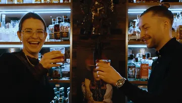 Zwei Menschen lächeln mit Getränken in einer Bar.