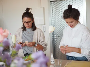 Zwei Frauen gestalten florale Arrangements am Tisch.