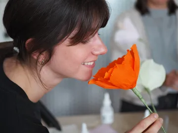 Frau riecht an orangefarbener Blume in geschäftigem Raum.