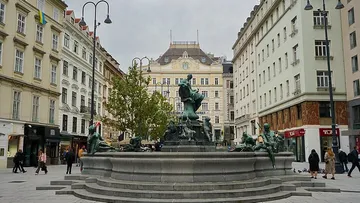 Fountain in plaza surrounded by buildings, overcast sky.