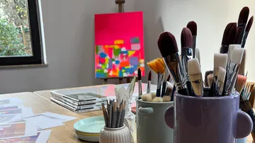 Brushes in containers, abstract painting on easel.