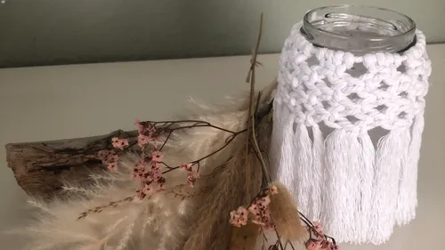 Glas mit Makramee-Überzug auf Tisch.