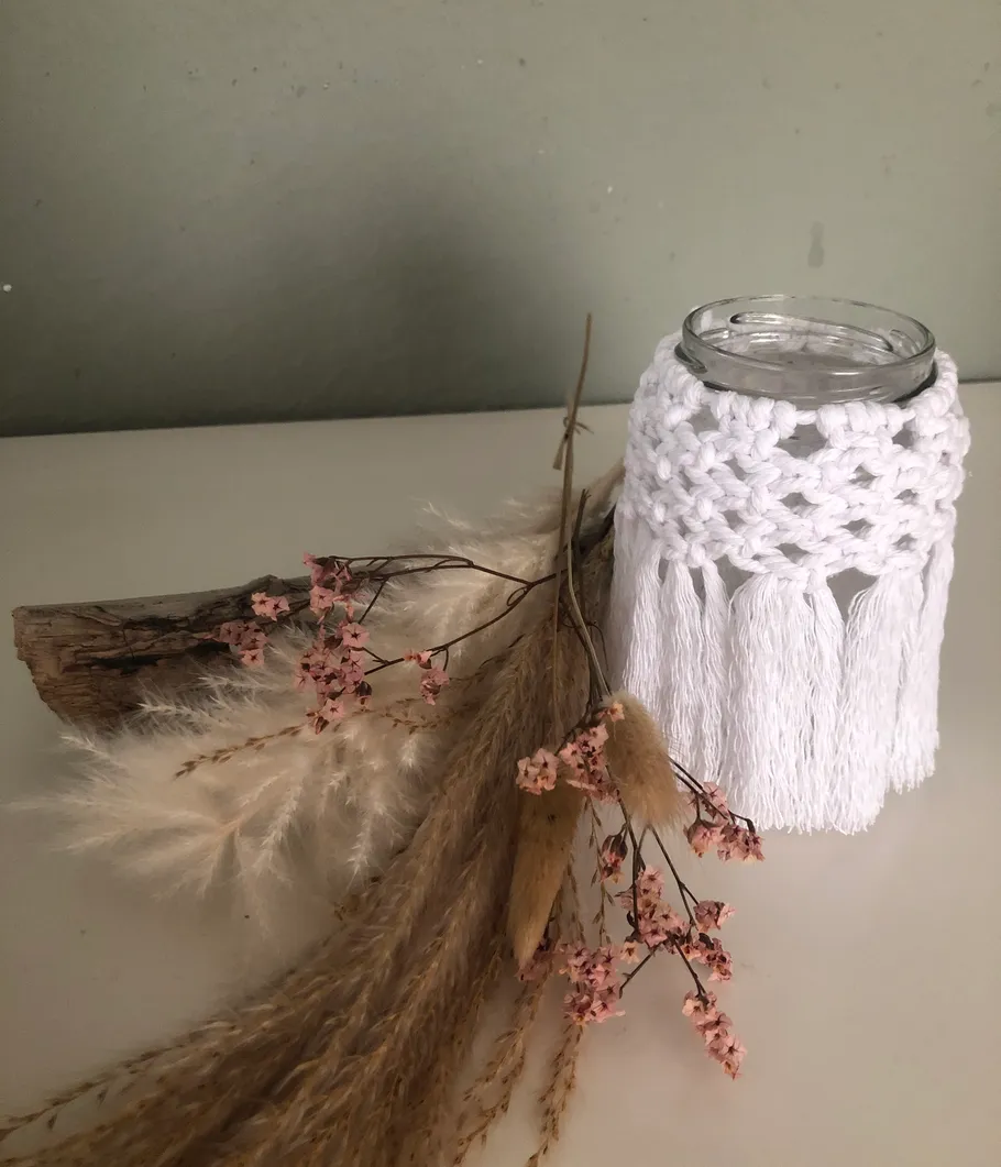 Macrame-covered jar with dried flowers on table.