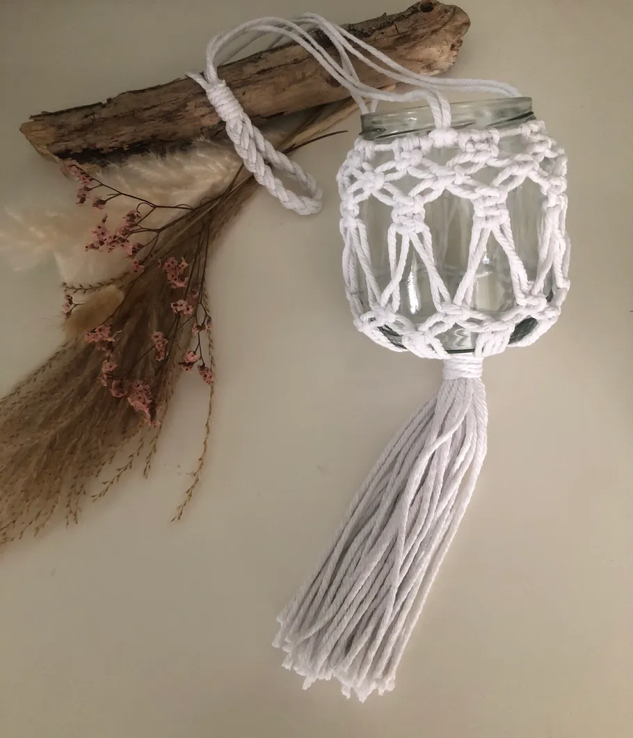 Macramé jar hanging from driftwood, with dried flowers.