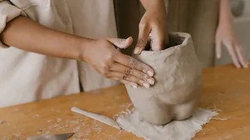 Hände formen Tonvase auf Tisch.