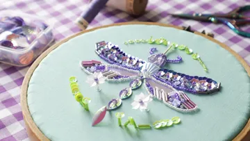 Perlengestickte Libelle auf grünem Stoff.