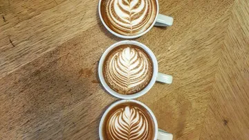 Three lattes with art on wooden table.