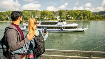 Couple watches ferry on river from railing.