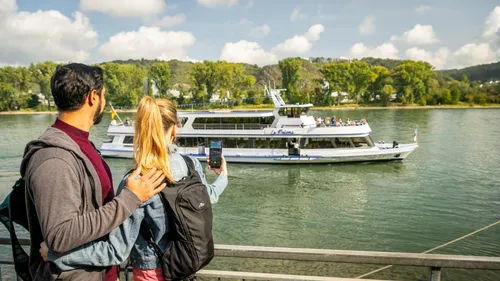 Couple watching boat on river, scenic background.