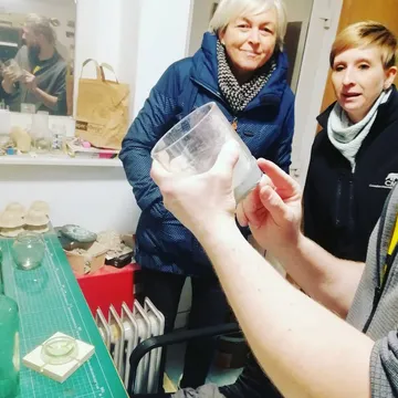 Person examining cup, two people observing, indoors.