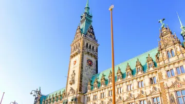 Historisches Gebäude mit Uhrturm, sonniger Tag.