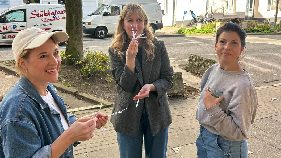 Drei Frauen halten Papierstreifen im Freien.