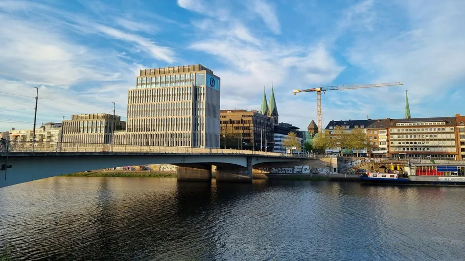 Brücke über Fluss mit modernen Gebäuden und Kränen.